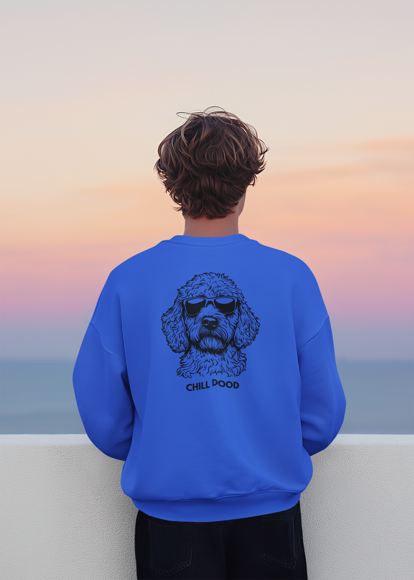 Person wearing a blue sweatshirt with a dog graphic and 'Chill Pood' text, standing against a sunset sky.